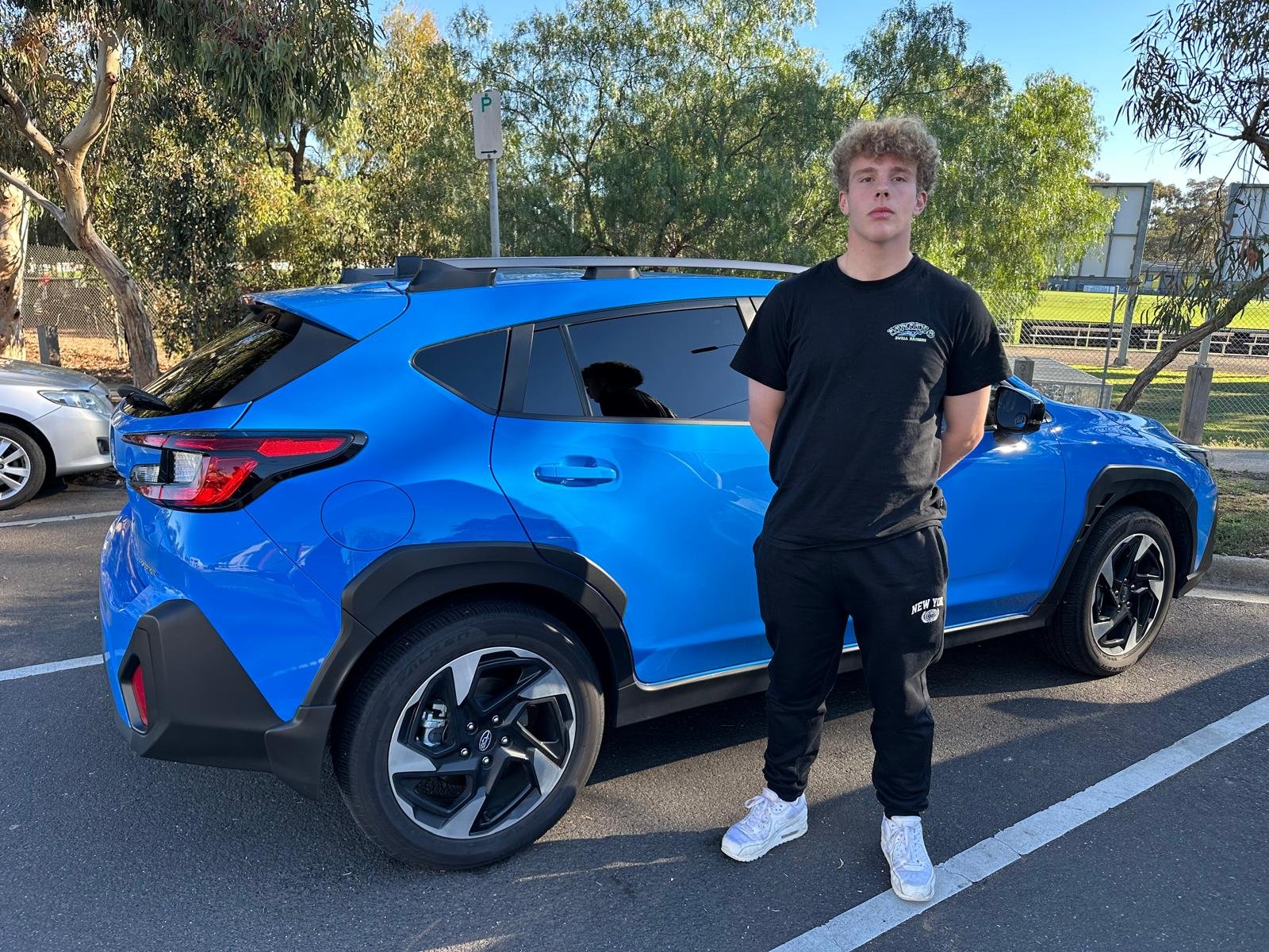 A learner standing beside the blue Washington’s Drive School Subaru